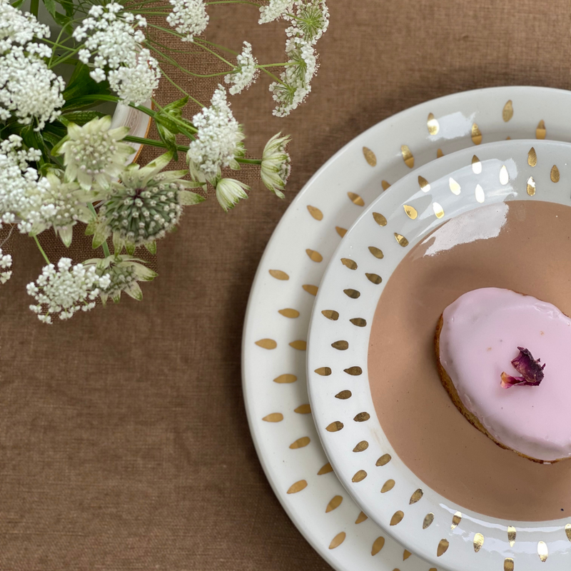 Handmade ceramic plates in beige with white rim and gold patterns looking like a sun